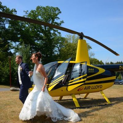 Ein Brautpaar läuft an einem Gelben AirLloyd Helikopter vorbei.