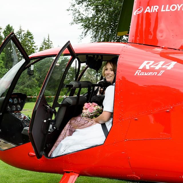 Eine Braut sitzt in einem roten AirLloyd Helikopter.