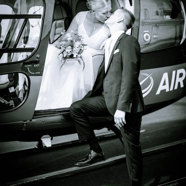 Schwarz-weißes Bild eines küssenden Brautpaares vor einem Helikopter.