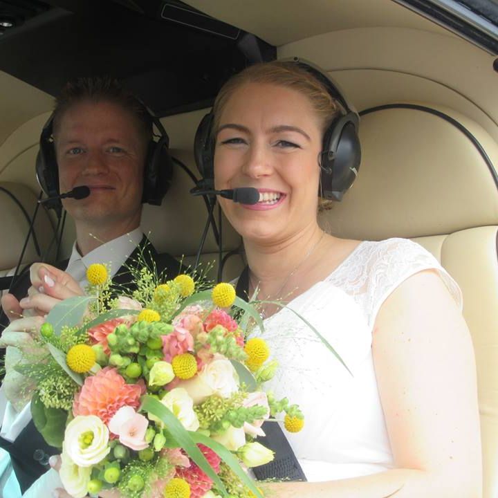 A bridal couple with flowers sits in a helicopter.