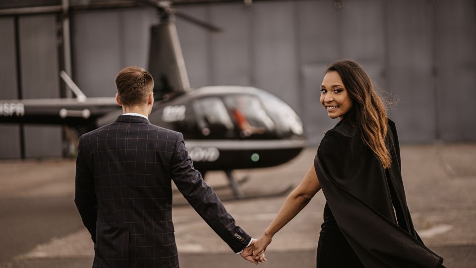 A couple stands holding hands in front of a black Air Lloyd helicopter