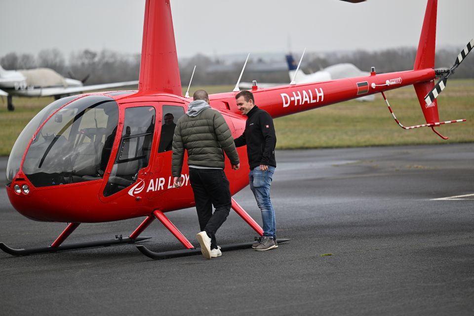 Two people stand in front of a red Air Lloyd helicopter