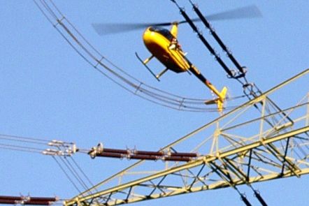 Ein gelber Hubschrauber fliegt über Stromleitungen.