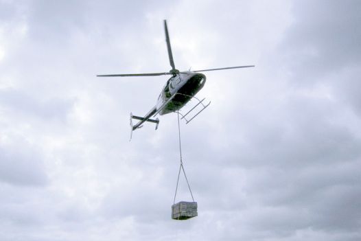 A crate is lifted from the ground by a helicopter.