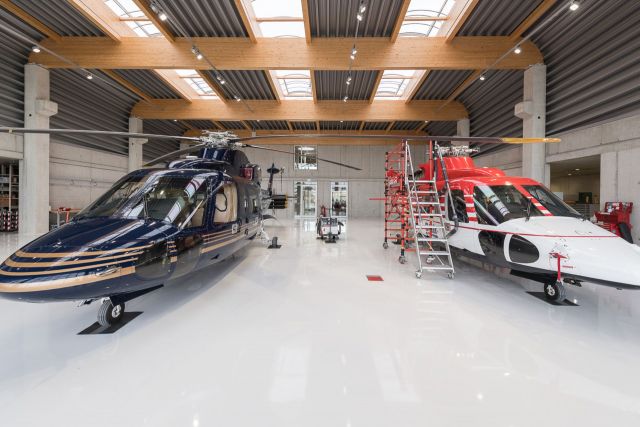 Ein blauer und ein rot-weißer Helikopter im Hangar.