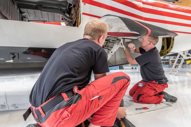 Two men working on a red and white helicopter.