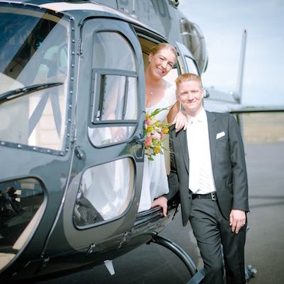 A bridal couple poses in front of a black helicopter.