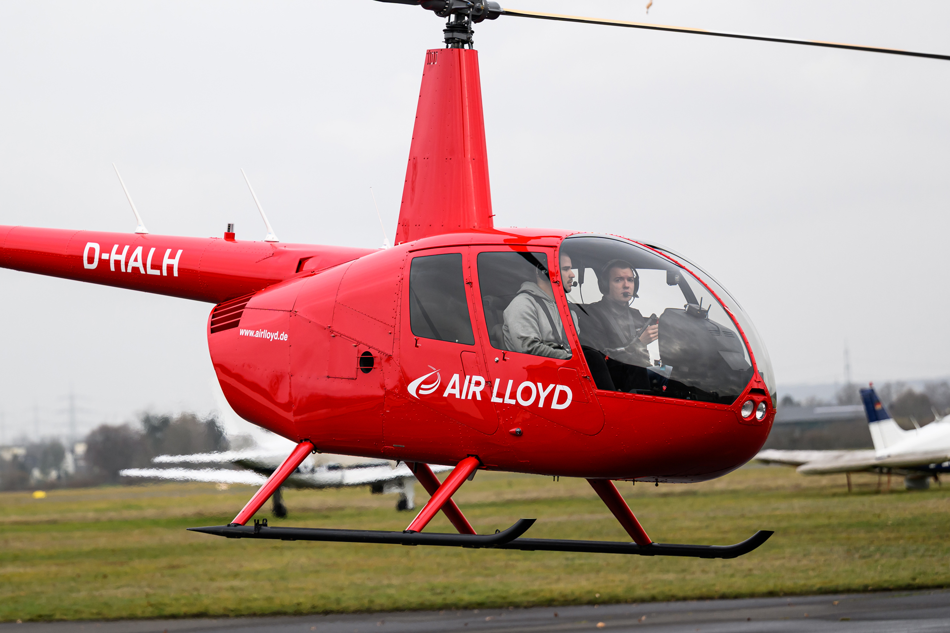 Ein roter Air Lloyd Helikopter mit Pilot beim Abflug