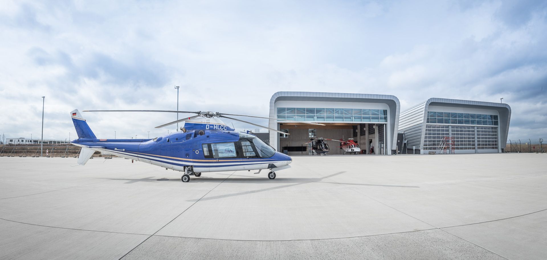 Ein blauer Hubschrauber steht vor einem Hangar.